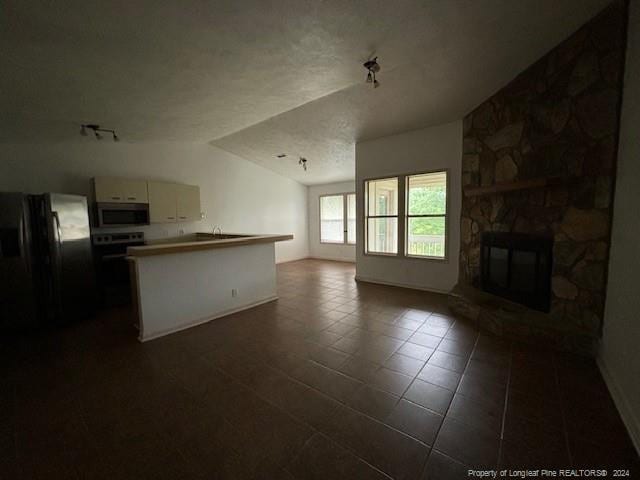 unfurnished living room with a fireplace, dark tile patterned floors, and vaulted ceiling