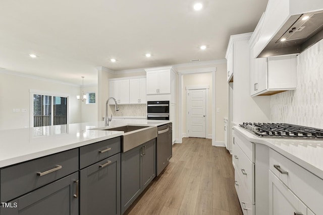 kitchen featuring appliances with stainless steel finishes, pendant lighting, white cabinetry, sink, and custom exhaust hood