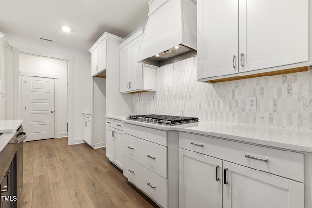 kitchen featuring custom exhaust hood, white cabinetry, stainless steel gas cooktop, and decorative backsplash