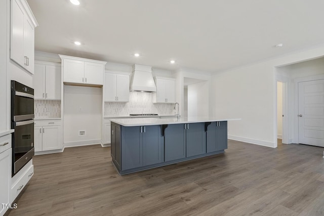 kitchen featuring custom exhaust hood, a kitchen island with sink, and white cabinets