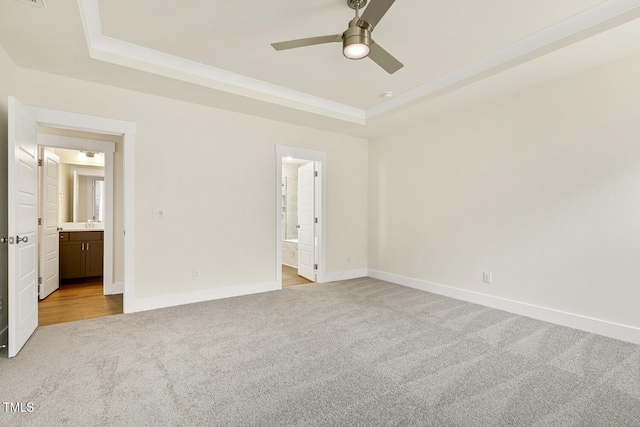 unfurnished bedroom with ceiling fan, ensuite bath, a tray ceiling, and light carpet