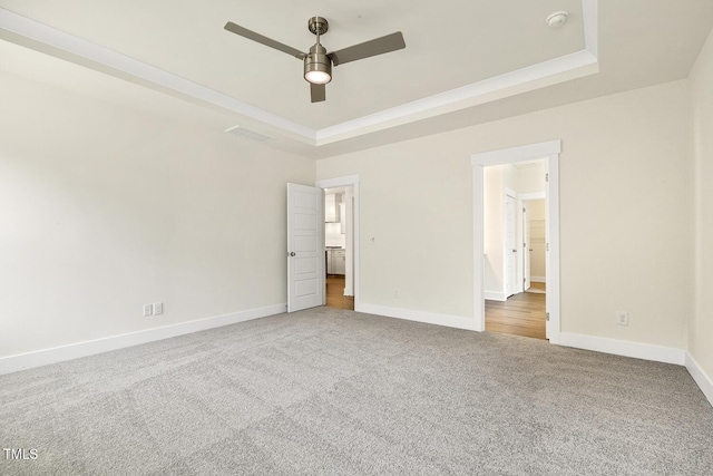 unfurnished bedroom with ceiling fan, a tray ceiling, and carpet