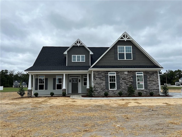 craftsman house featuring a shingled roof, stone siding, and a porch