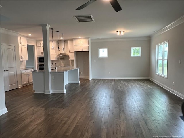 kitchen with backsplash, dark wood-type flooring, white cabinets, and a kitchen island with sink