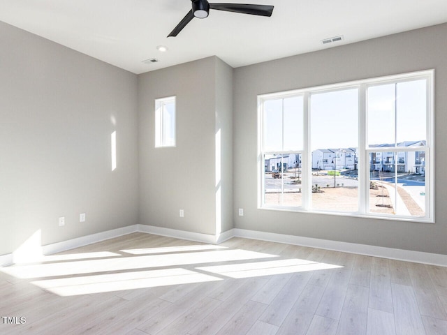 empty room with a wealth of natural light, ceiling fan, and light hardwood / wood-style flooring