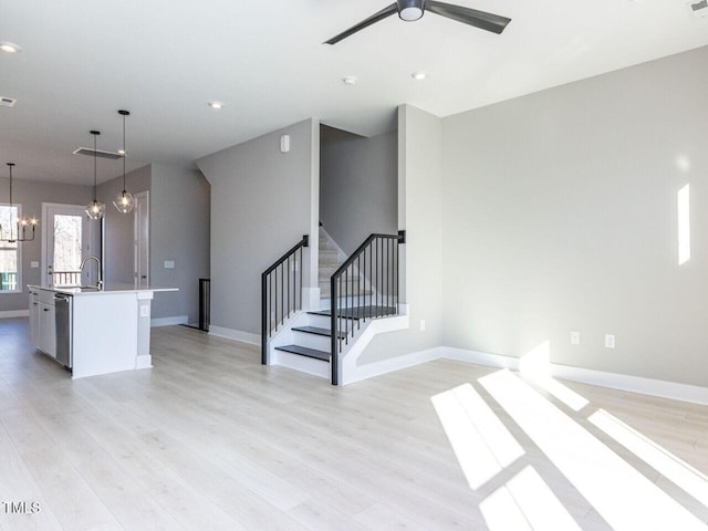 unfurnished living room with ceiling fan with notable chandelier, light hardwood / wood-style floors, and sink