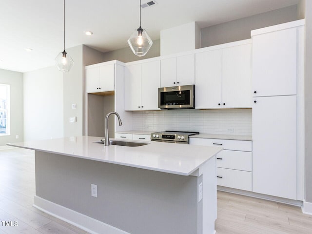 kitchen with pendant lighting, sink, stainless steel appliances, and a center island with sink