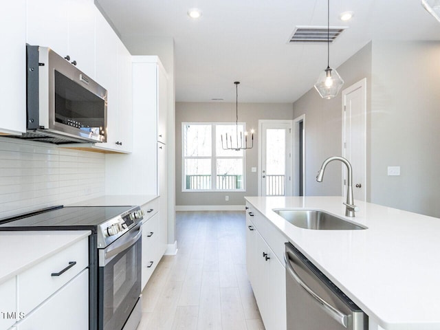 kitchen with sink, hanging light fixtures, stainless steel appliances, a center island with sink, and decorative backsplash