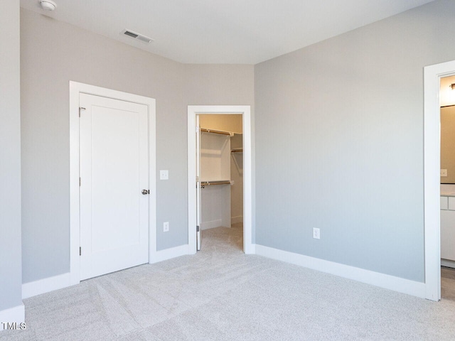 unfurnished bedroom with a walk in closet, ensuite bath, a closet, and light carpet