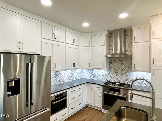 kitchen with wall chimney exhaust hood, sink, appliances with stainless steel finishes, white cabinets, and backsplash