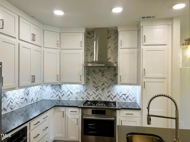 kitchen with sink, appliances with stainless steel finishes, white cabinetry, tasteful backsplash, and wall chimney exhaust hood