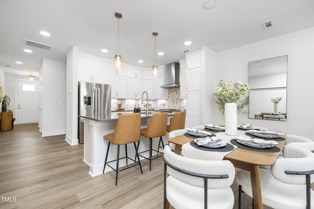 kitchen featuring hanging light fixtures, wall chimney range hood, white cabinetry, and visible vents