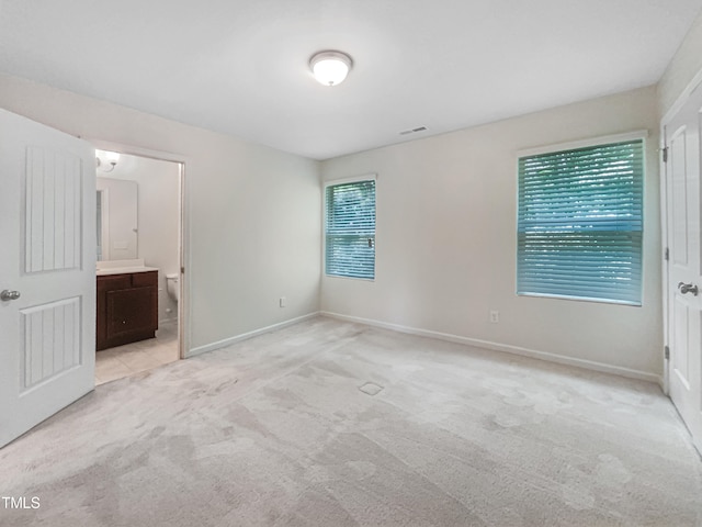 unfurnished bedroom featuring ensuite bathroom, multiple windows, and light colored carpet