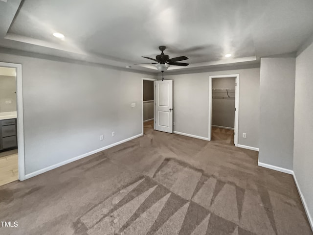 unfurnished bedroom with carpet, ensuite bathroom, a walk in closet, ceiling fan, and a closet