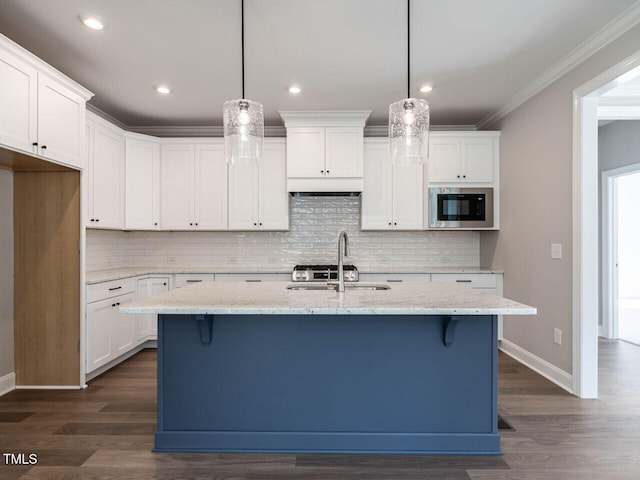 kitchen featuring pendant lighting, stainless steel microwave, a kitchen island with sink, dark wood-type flooring, and white cabinets