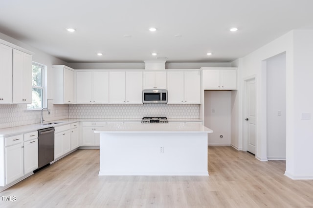 kitchen with sink, light hardwood / wood-style flooring, appliances with stainless steel finishes, white cabinets, and a kitchen island