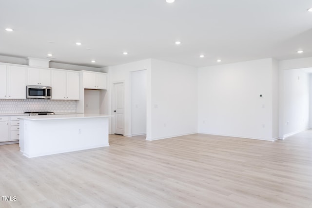 kitchen featuring white cabinetry, light wood-type flooring, a kitchen island with sink, and backsplash