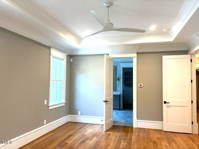 8305 Society Pl, Raleigh, NC 27615 - unfurnished bedroom featuring a tray ceiling, light wood finished floors, and ornamental molding