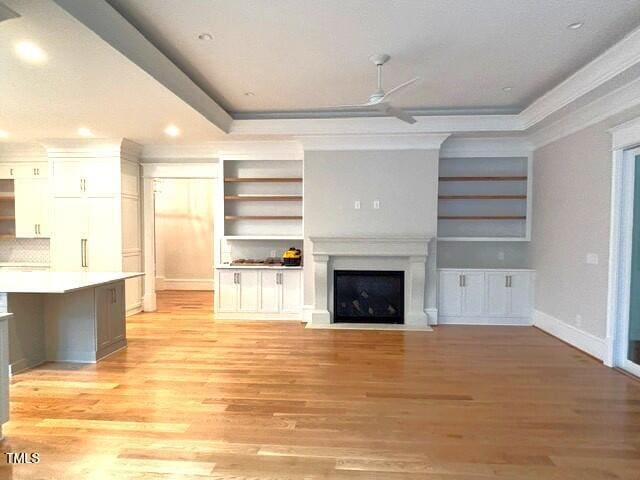8305 Society Pl, Raleigh, NC 27615 - unfurnished living room featuring a ceiling fan, a fireplace with flush hearth, a raised ceiling, light wood-style floors, and crown molding