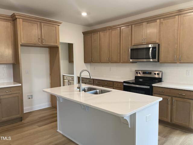 kitchen with backsplash, stainless steel appliances, sink, light hardwood / wood-style flooring, and an island with sink