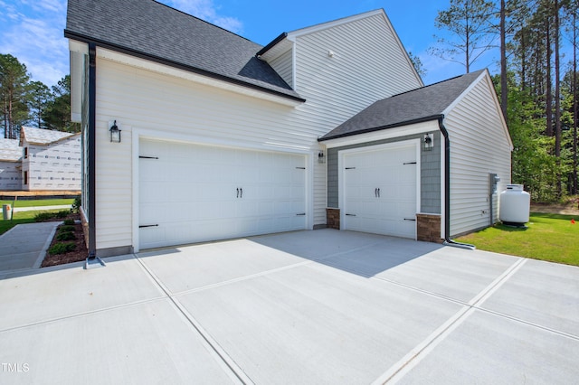 view of side of home with a garage, a shingled roof, driveway, and stone siding
