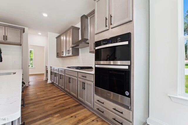 kitchen with double oven, wood finished floors, a wealth of natural light, and wall chimney range hood