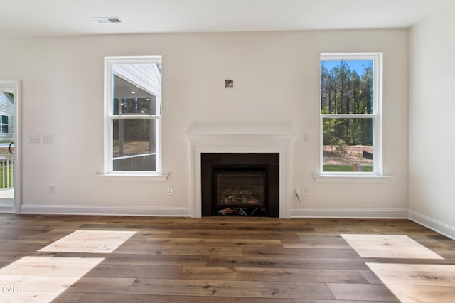 unfurnished living room featuring baseboards, a glass covered fireplace, wood finished floors, and visible vents