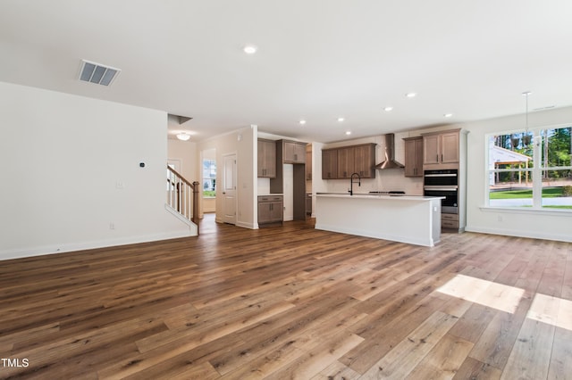 kitchen with wall chimney range hood, open floor plan, visible vents, and wood-type flooring