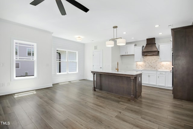 kitchen with premium range hood, a center island with sink, hanging light fixtures, and dark hardwood / wood-style floors