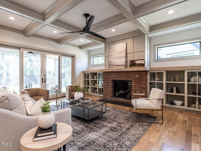 living room featuring coffered ceiling, a fireplace, light wood-type flooring, and plenty of natural light