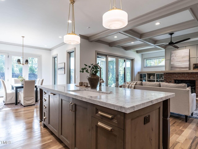 kitchen with light stone counters, a kitchen island with sink, light wood-type flooring, sink, and decorative light fixtures