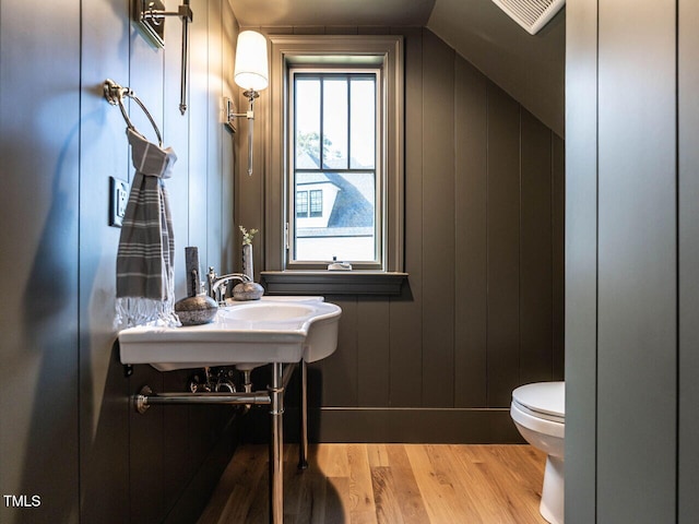 bathroom with toilet, wood walls, hardwood / wood-style flooring, and vaulted ceiling