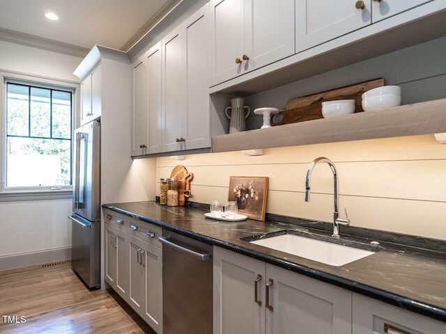 kitchen with dark stone countertops, stainless steel appliances, light hardwood / wood-style flooring, and sink