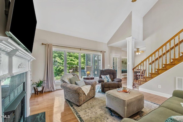 living room with stairway, high vaulted ceiling, a fireplace with flush hearth, and light wood finished floors