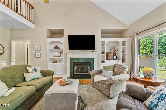 living area with a premium fireplace, high vaulted ceiling, built in features, and wood finished floors