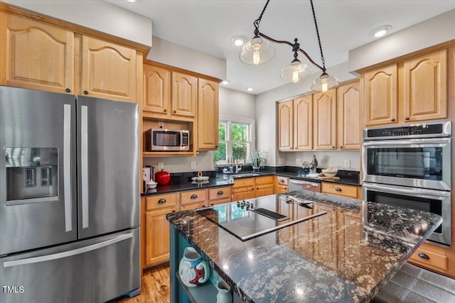 kitchen with light brown cabinetry, stainless steel appliances, dark stone countertops, and a center island