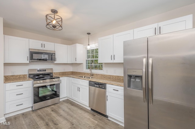 kitchen featuring appliances with stainless steel finishes, decorative light fixtures, sink, white cabinets, and light stone countertops