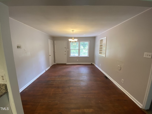 unfurnished dining area featuring built in shelves, dark wood-type flooring, and a notable chandelier