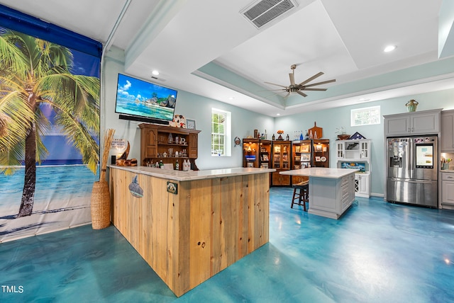 kitchen featuring ceiling fan, a raised ceiling, a kitchen island, gray cabinetry, and stainless steel fridge with ice dispenser