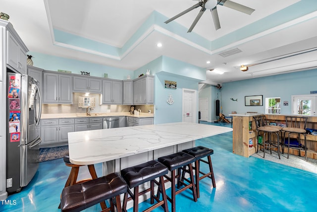 kitchen featuring stainless steel appliances, ceiling fan, a raised ceiling, a kitchen bar, and gray cabinets