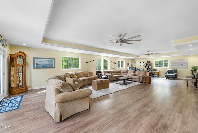 living room with ceiling fan, a tray ceiling, and light wood-type flooring