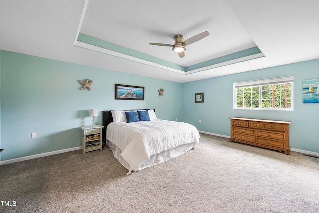 carpeted bedroom with ceiling fan and a tray ceiling