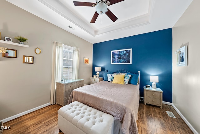 bedroom with dark hardwood / wood-style flooring, ceiling fan, and a raised ceiling