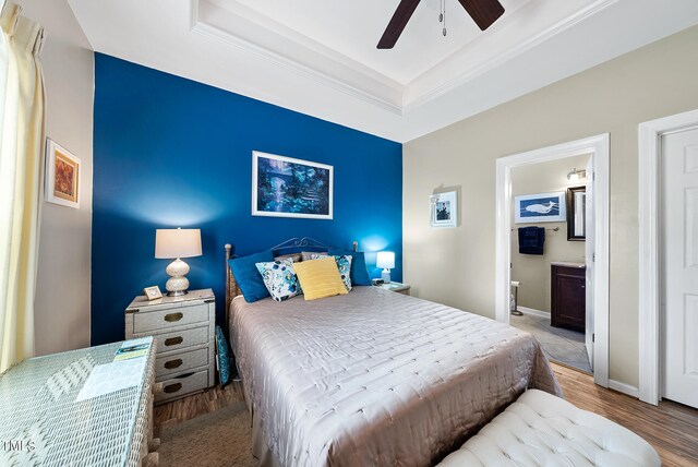 bedroom with wood-type flooring, ceiling fan, ensuite bath, and a tray ceiling