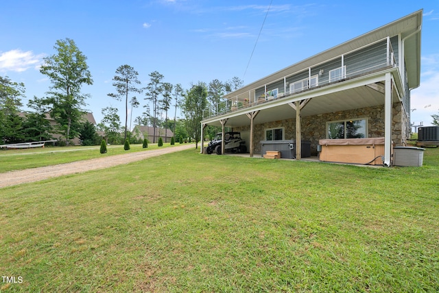 rear view of house featuring a hot tub, a balcony, central air condition unit, and a lawn