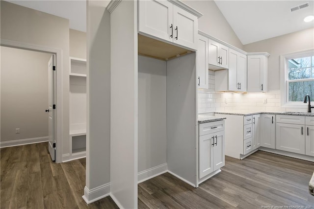 kitchen featuring dark hardwood / wood-style flooring, white cabinetry, lofted ceiling, and light stone counters