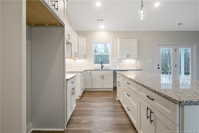 kitchen with sink, hanging light fixtures, a kitchen island, white cabinets, and backsplash