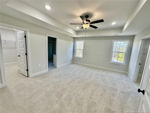 unfurnished bedroom with a closet, a walk in closet, light carpet, and a tray ceiling