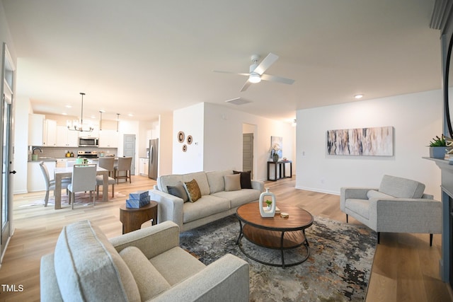 living room with ceiling fan with notable chandelier, sink, and light hardwood / wood-style flooring