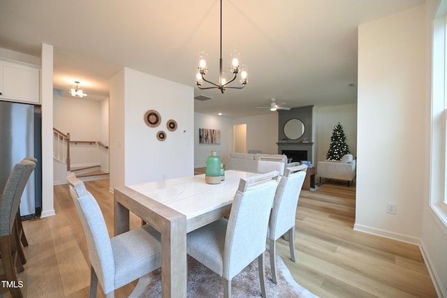 dining space with a fireplace, light hardwood / wood-style floors, and ceiling fan with notable chandelier